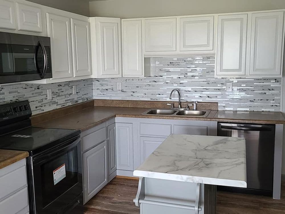 Modern kitchen with gray cabinets, marble island, stainless steel appliances, and tiled backsplash.