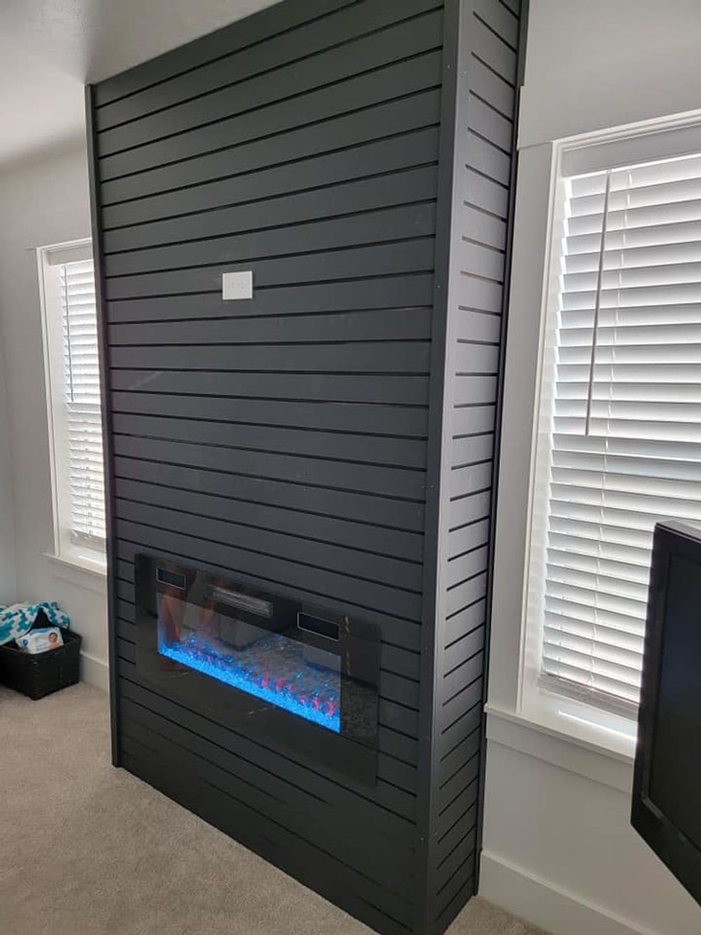 Modern wall-mounted electric fireplace with blue LED lights and sleek black wood paneling.