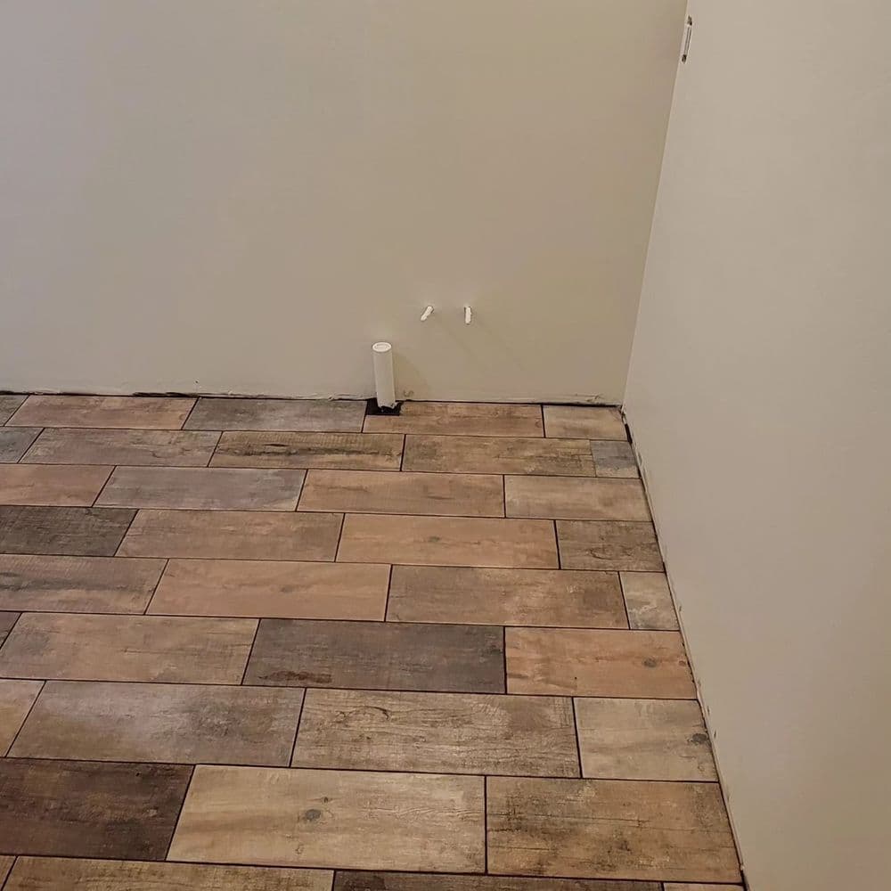 Newly installed wooden tile flooring with wall pipe fittings in an empty room.