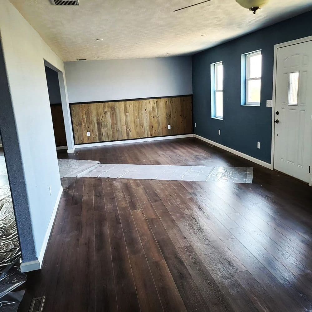Spacious living room with wood flooring and blue walls, featuring natural light from windows.