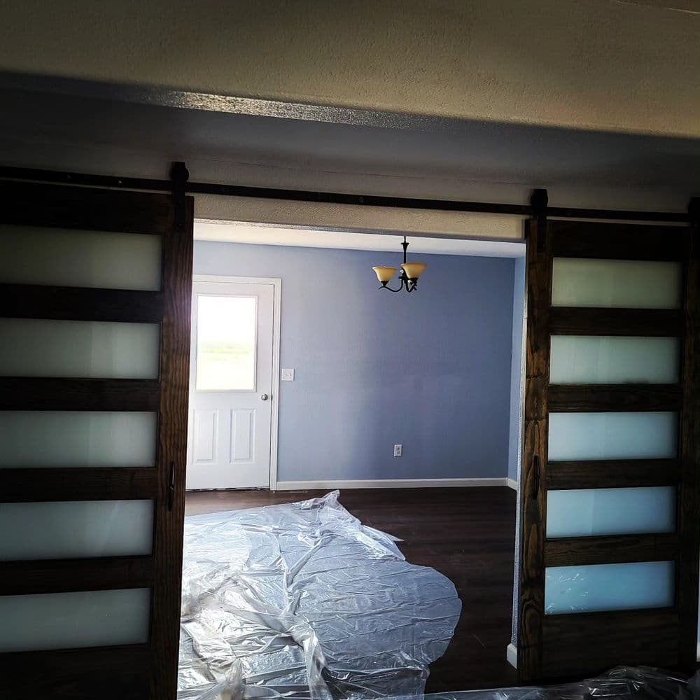 Interior view of a room with sliding barn doors, freshly painted walls, and hardwood floors.
