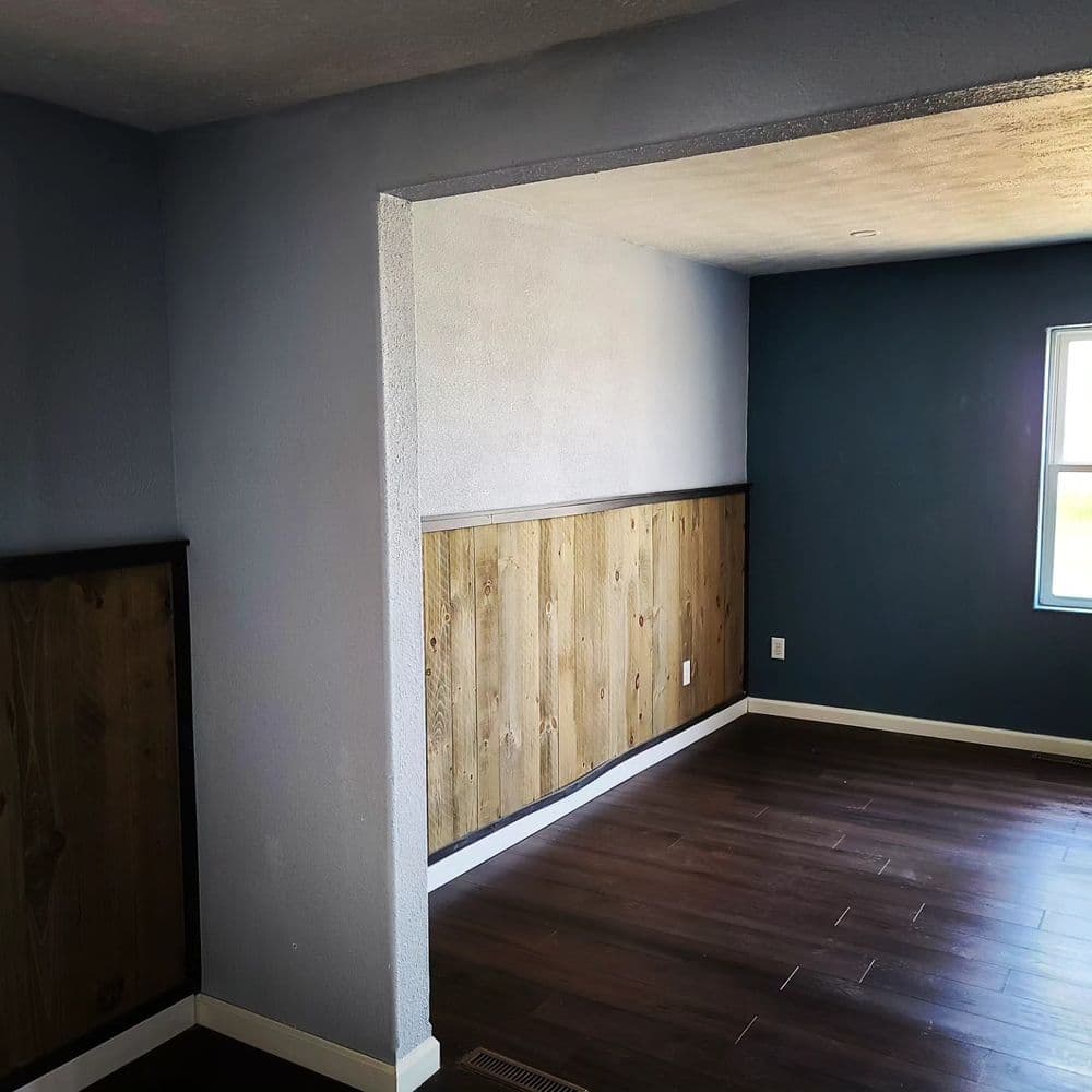 Room interior featuring blue and wooden walls with dark wooden flooring and natural light.