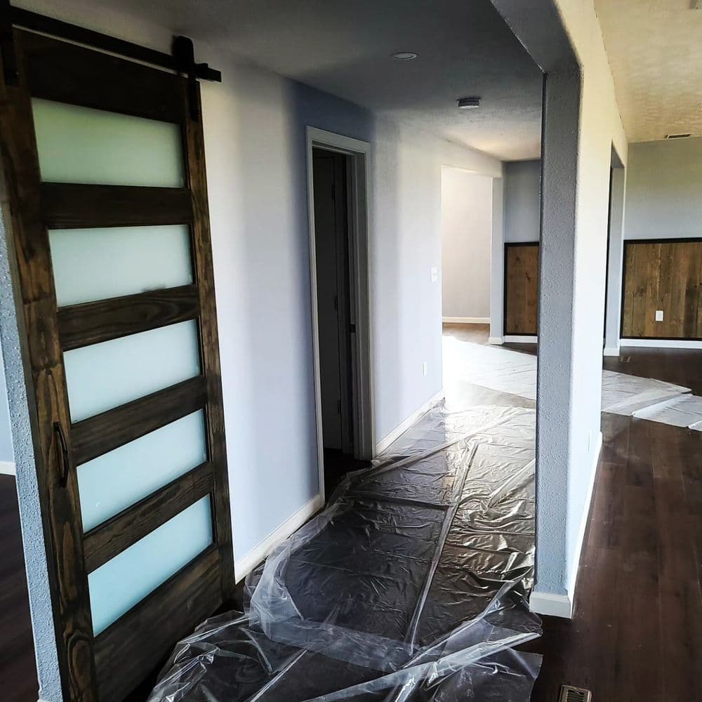 View of a modern hallway featuring a sliding barn door and protective plastic sheeting on the floor.