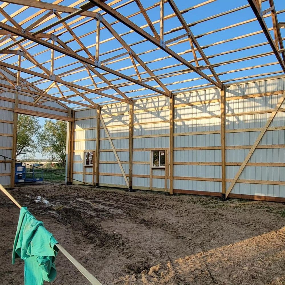 Interior view of an unfinished barn structure with wooden beams and dirt floor.
