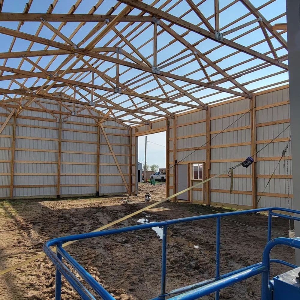Interior of a partially constructed barn with wooden framing and blue scaffolding visible.
