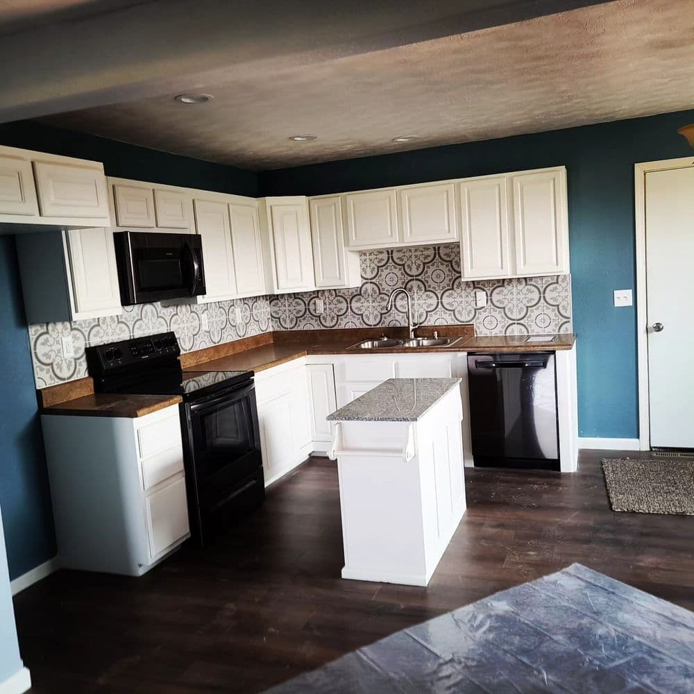 Modern kitchen with white cabinets, granite island, black appliances, and patterned backsplash.
