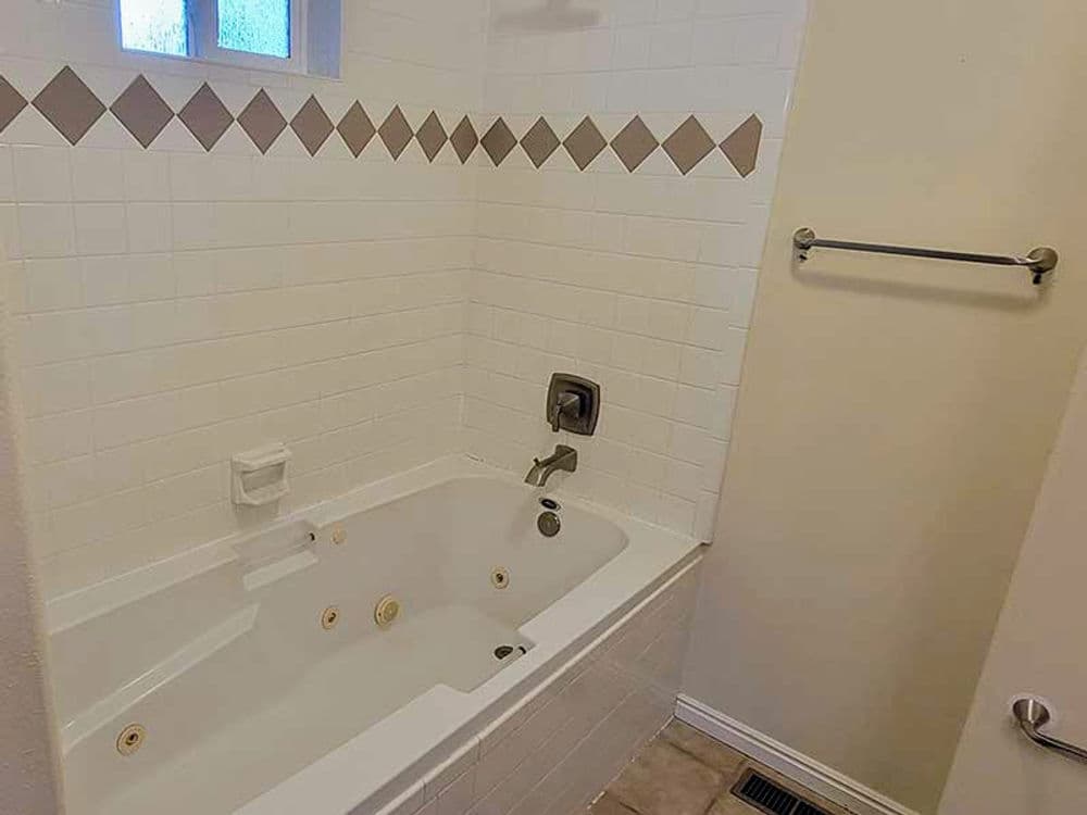 Modern bathroom featuring a white tiled jacuzzi tub with beige accents.