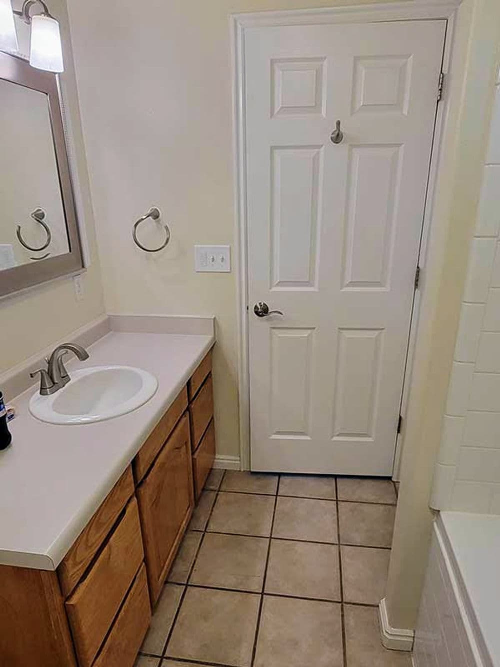 Bathroom featuring beige walls, wood cabinets, sink, and a door leading to another room.