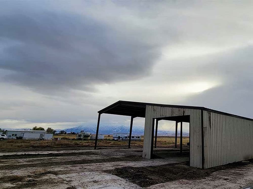 Industrial building frame against cloudy sky and mountain backdrop in rural landscape.