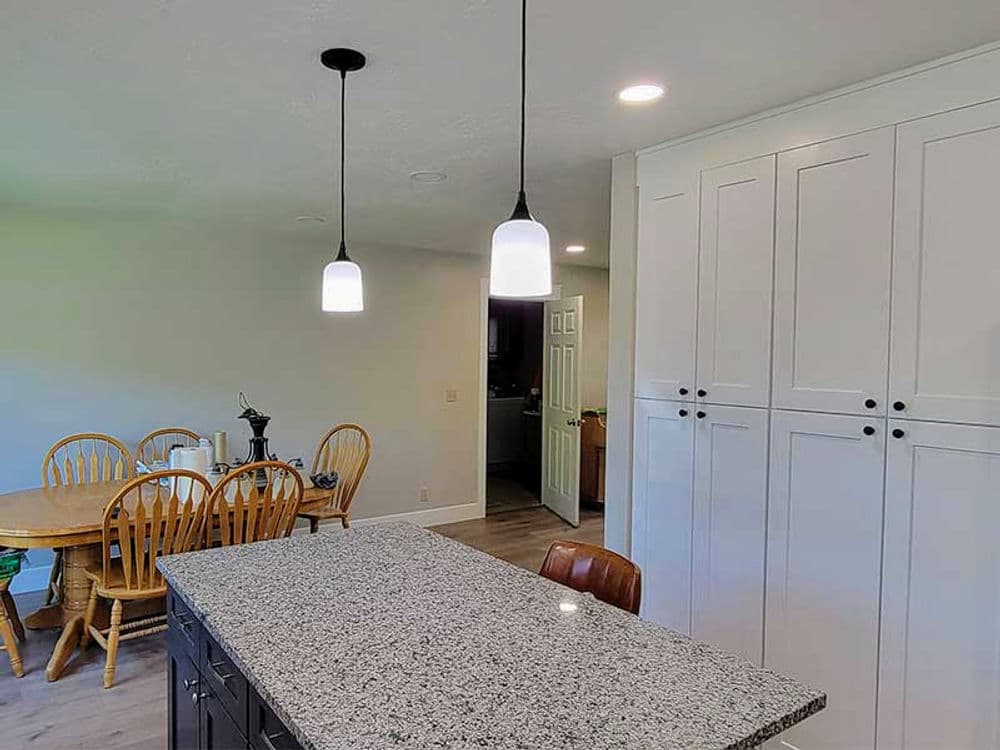 Modern kitchen with granite island, pendant lights, and a wooden dining table. Bright and spacious design.