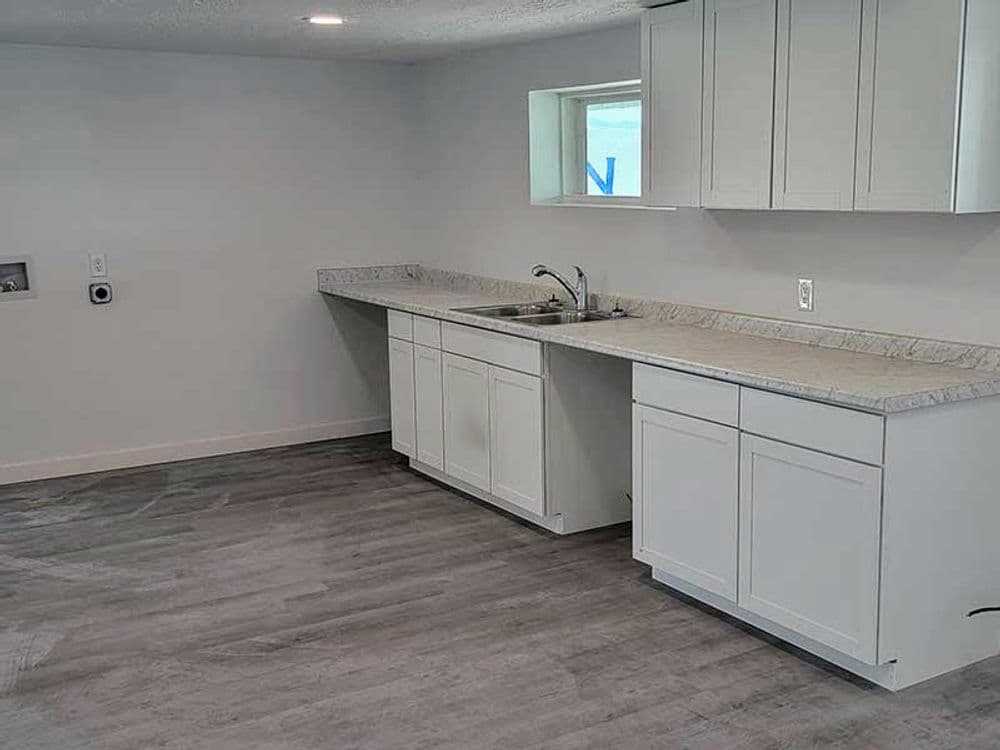 Modern kitchen interior with white cabinets, granite countertops, and vinyl flooring.
