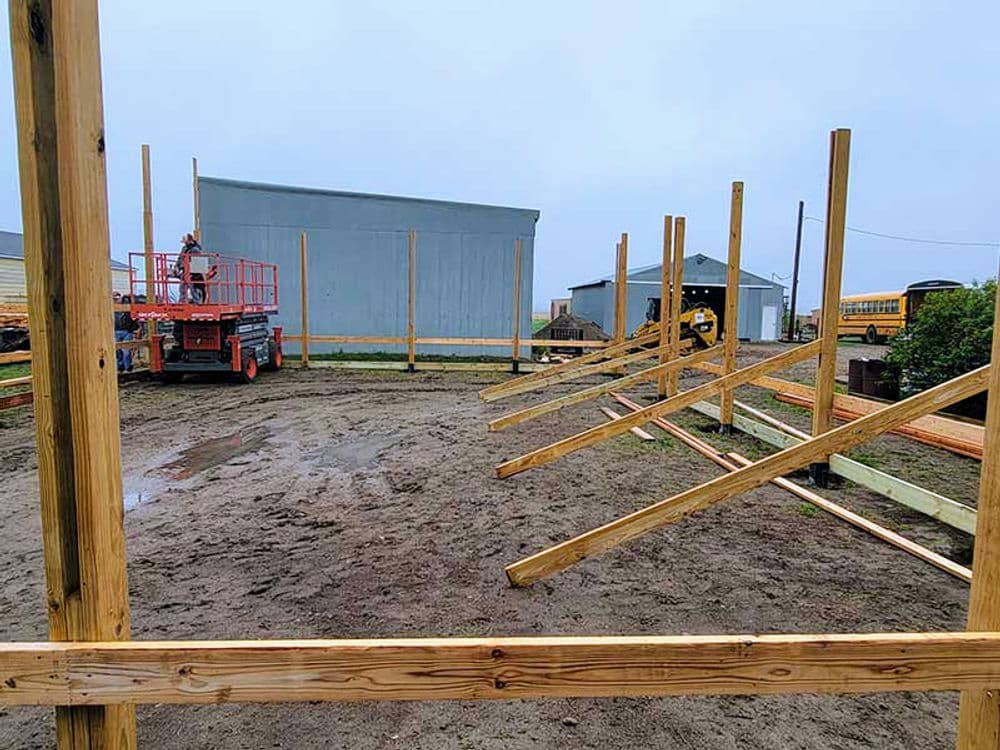 Construction site with wooden posts and machinery, preparing a structure on a muddy ground.