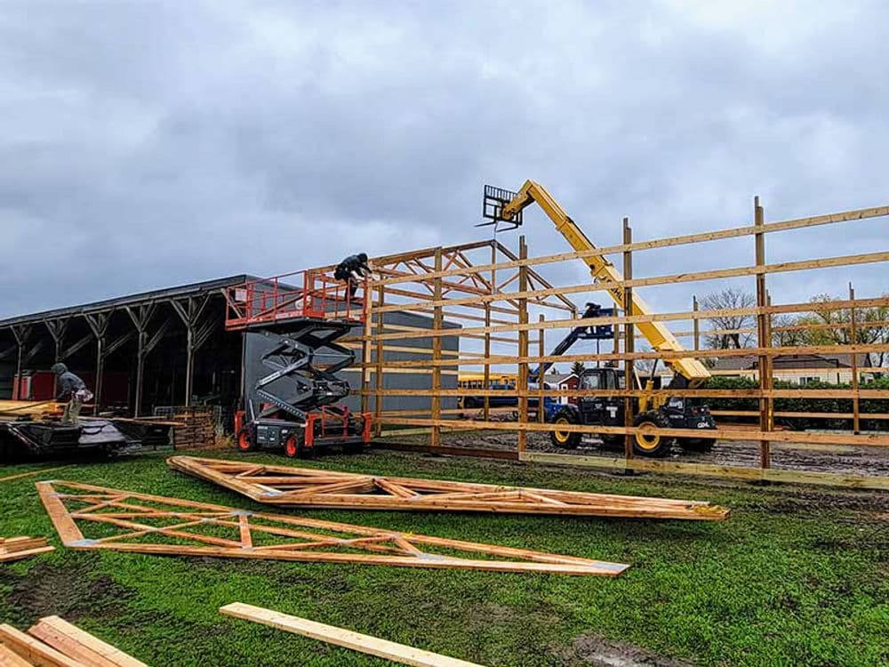 Construction workers using a telehandler to build a wooden frame structure on a cloudy day.