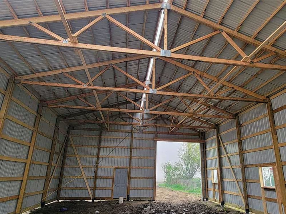 Interior of a spacious wooden barn with metal roofing and exposed beams, showcasing construction details.