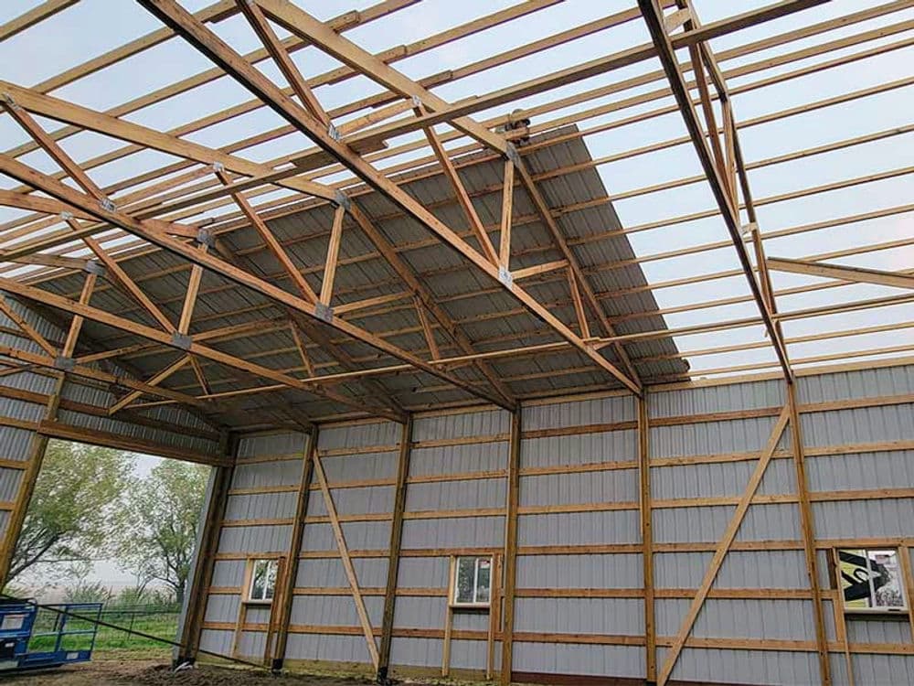 Interior view of a partially constructed building showcasing exposed wooden trusses and metal walls.