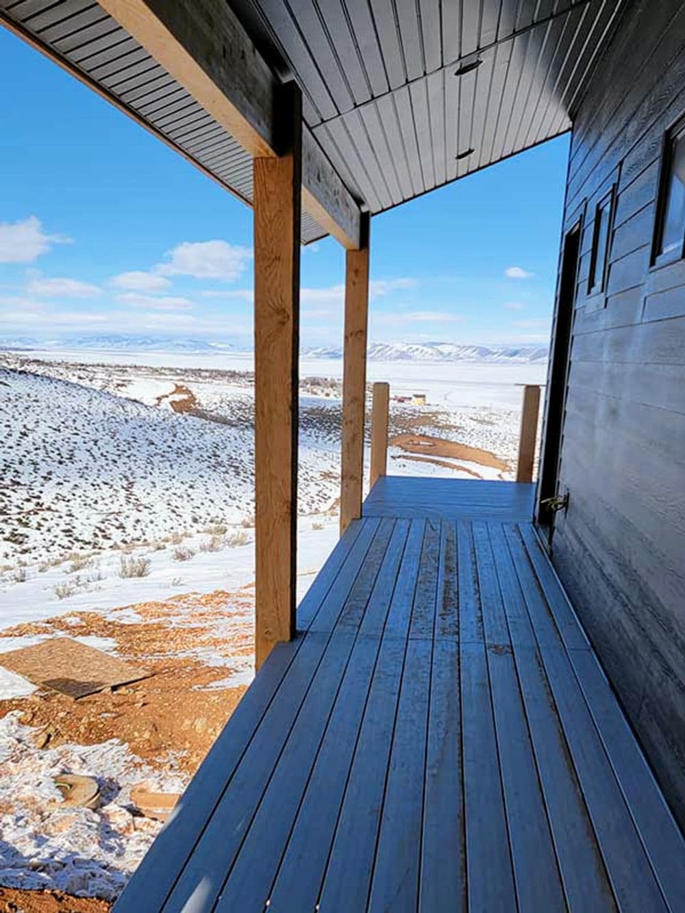 View from a modern deck overlooking snowy landscape and distant mountains under a clear blue sky.