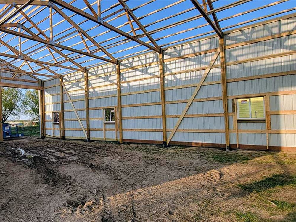 Construction of a steel barn showing interior framework and windows under clear blue sky.