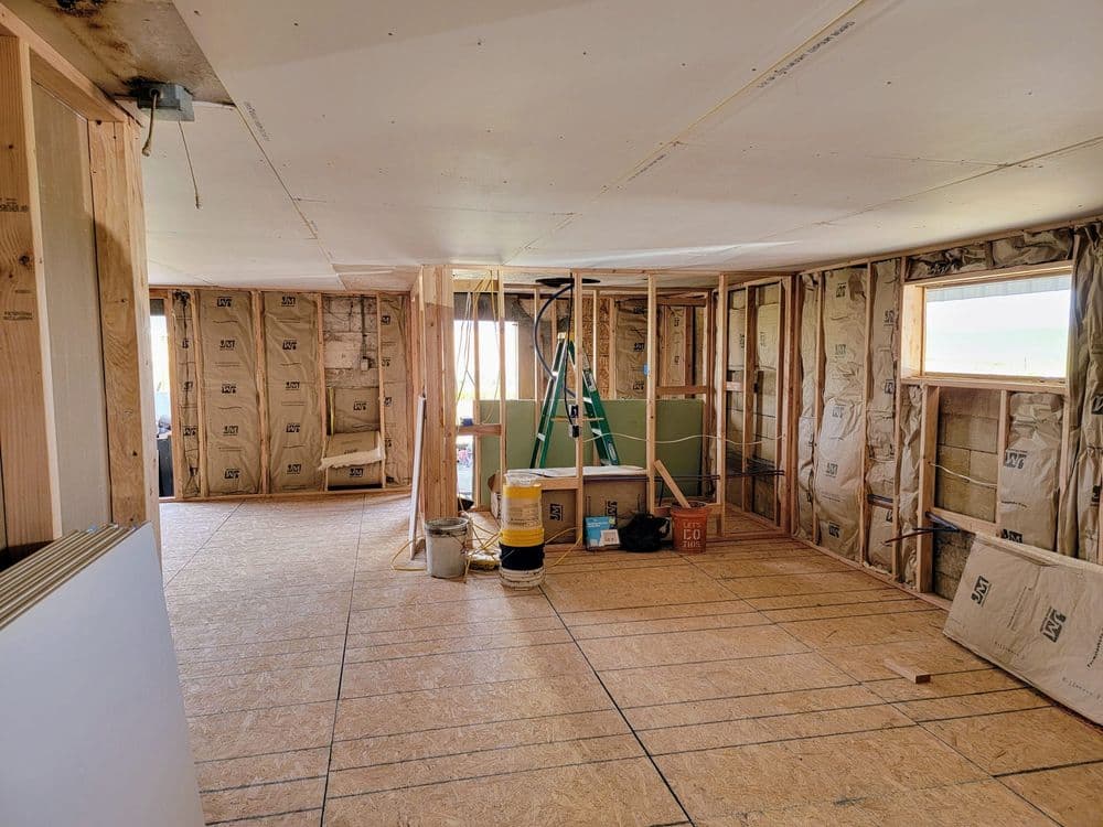 Interior construction zone showing framed walls, insulation, and a ladder in a remodel project.