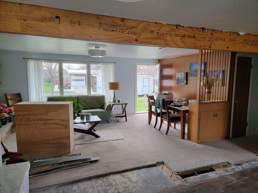 Open concept living room and dining area with green sofa, wooden dining furniture, and large windows.