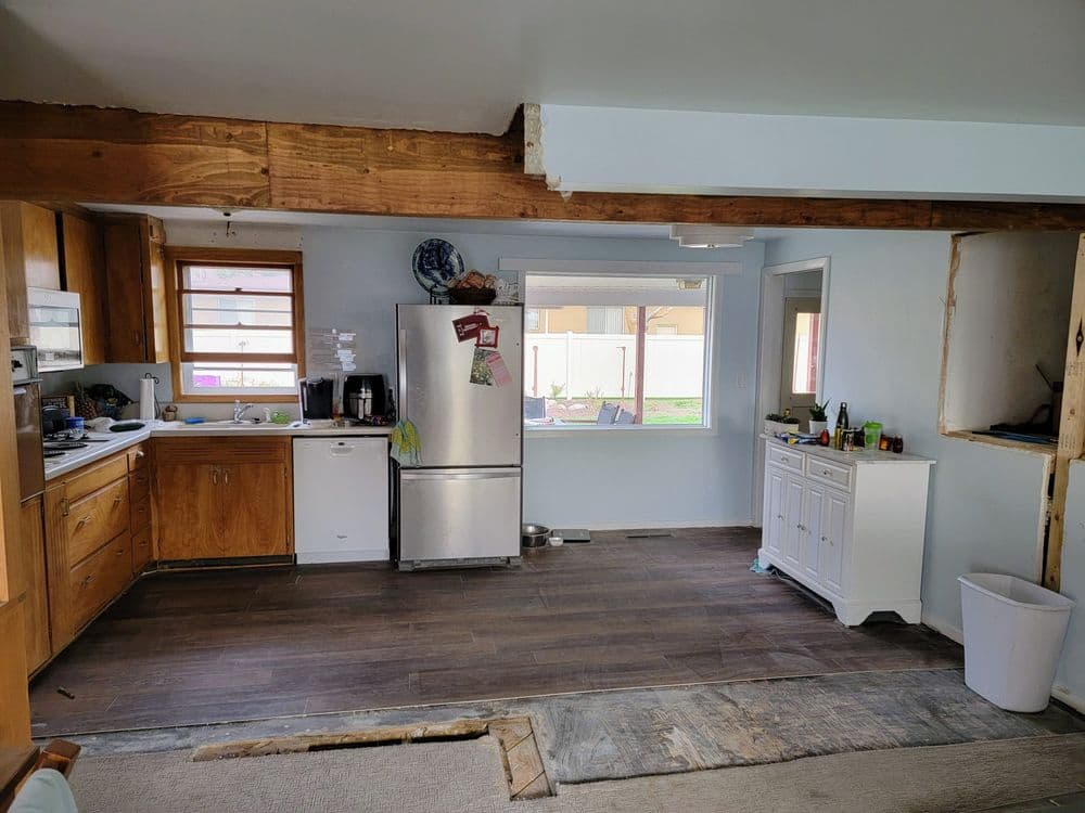 Renovated kitchen with wooden beams, modern appliances, and unfinished flooring.