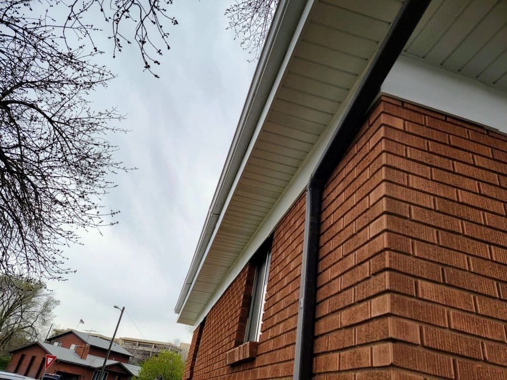 Close-up of a brick house's eaves and gutter against a cloudy sky.