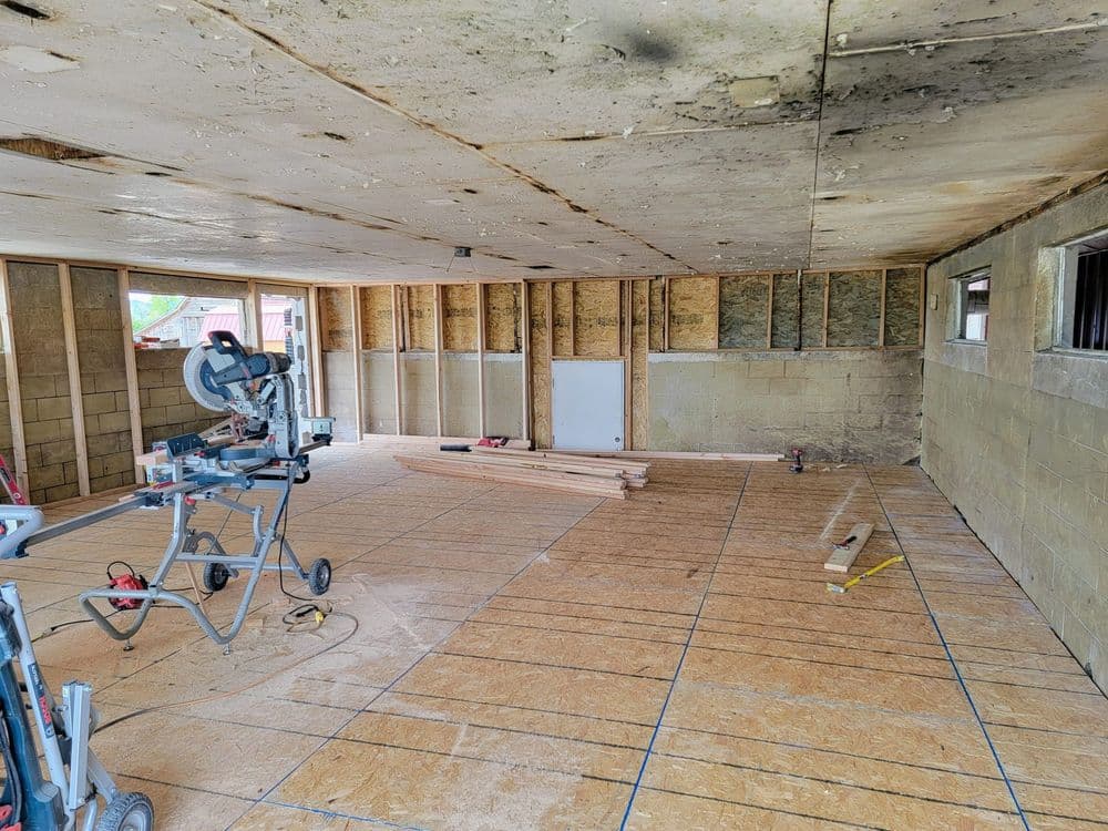Interior view of a construction site with wooden beams, tools, and exposed walls.