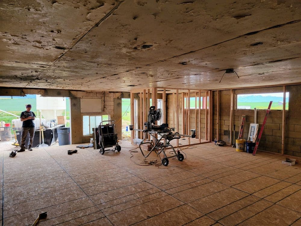 Construction site with framed walls, tools, and a worker in a partially renovated interior.